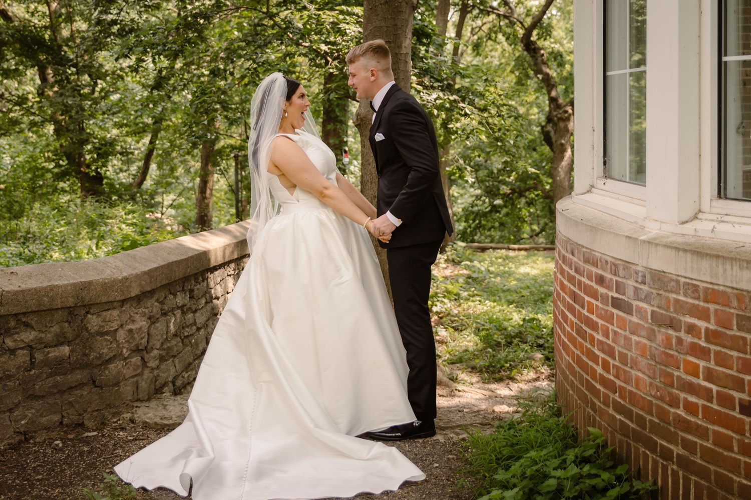 A wedding couple shares intimate moments in a garden setting with brick walls and lush greenery.