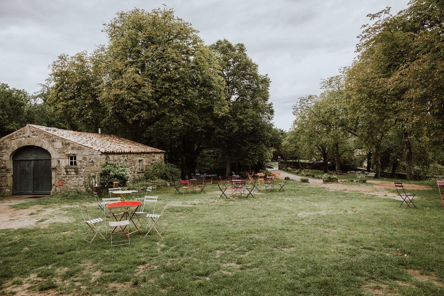 A panoramic view of a rustic stone building in a green meadow surrounded by autumn trees and wooden fencing.