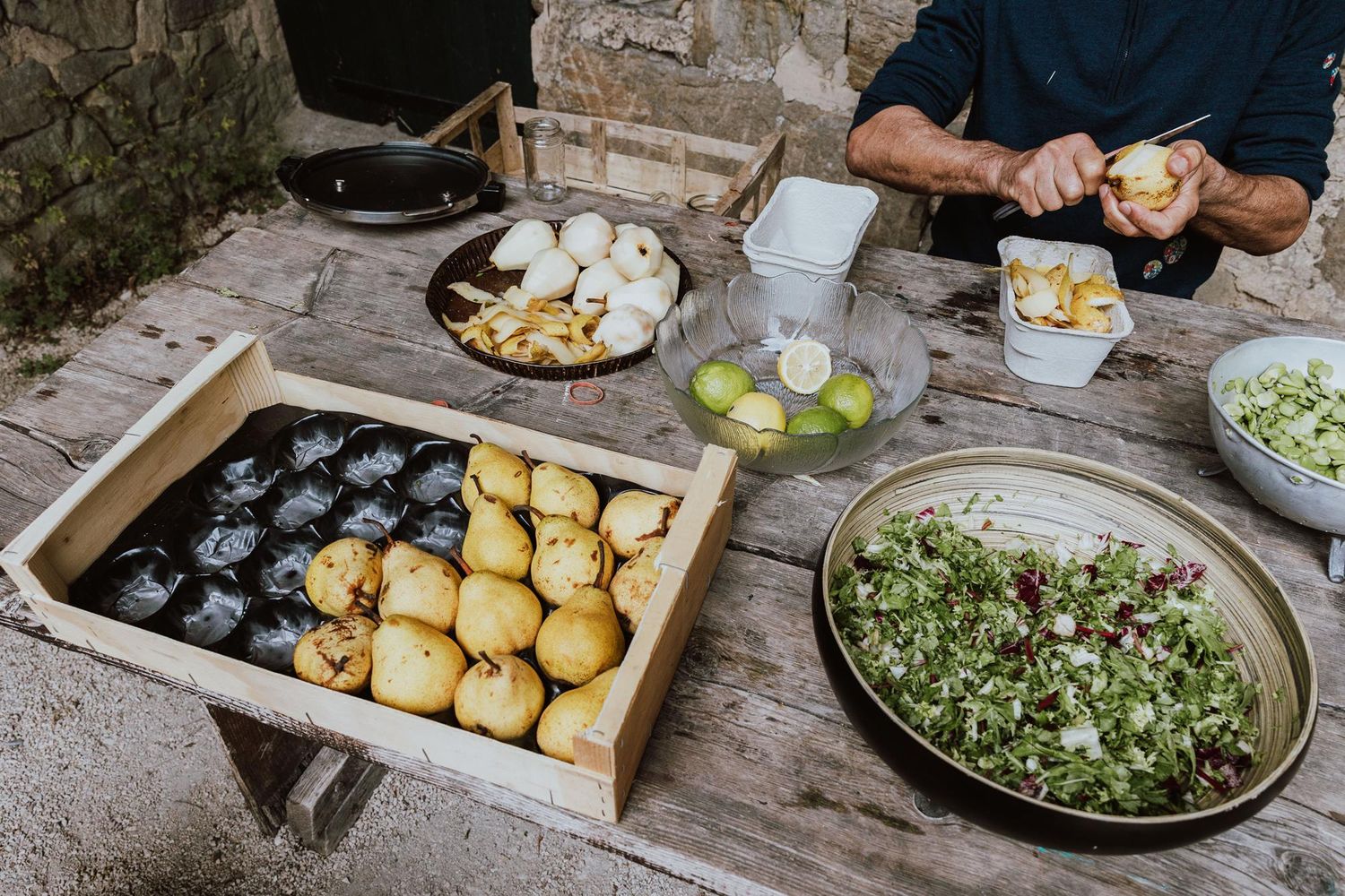Overhead view of a rustic table with fresh ingredients including potatoes, herbs, and vegetables being prepared for cooking.