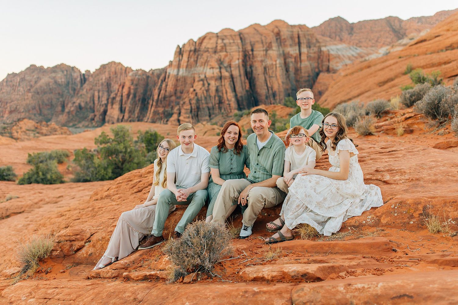 Family portrait session on red rock formations in desert setting during golden hour.