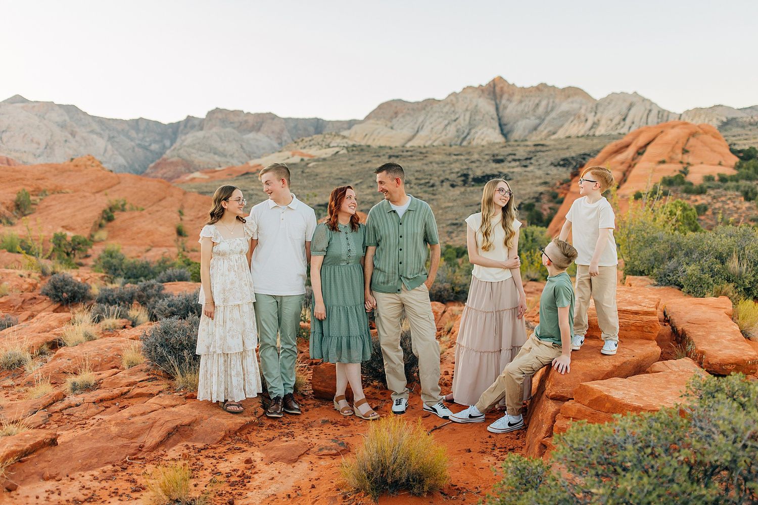 Group photo on red rock formations wearing coordinated outfits in sage green and cream colors.