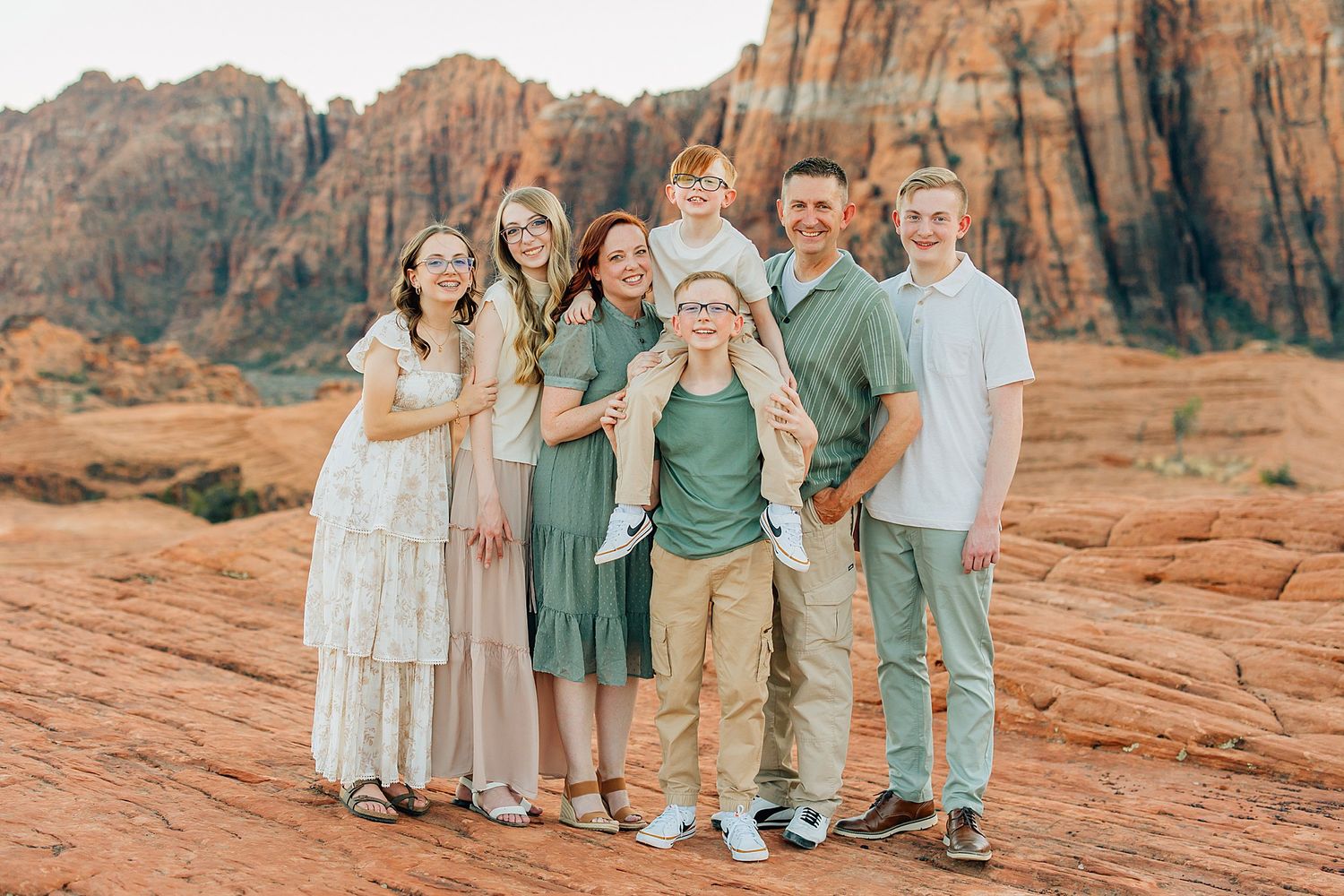 Family group standing together on red rock formations wearing coordinated green and neutral tones.