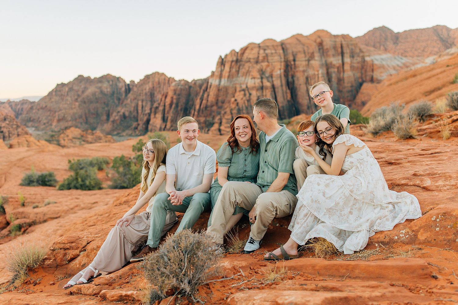 Group sitting casually on red rocks with dramatic desert canyon landscape behind them.