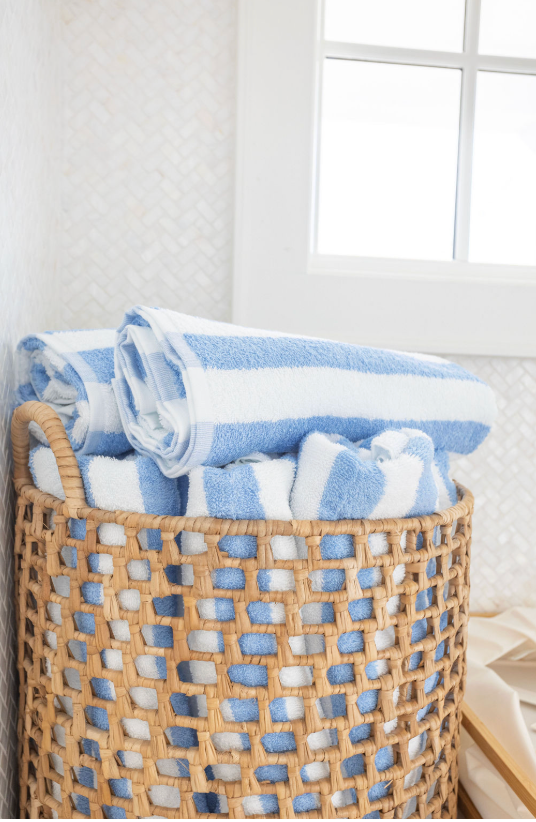 Folded blue towels neatly arranged in woven wicker storage baskets against a white wall with window.