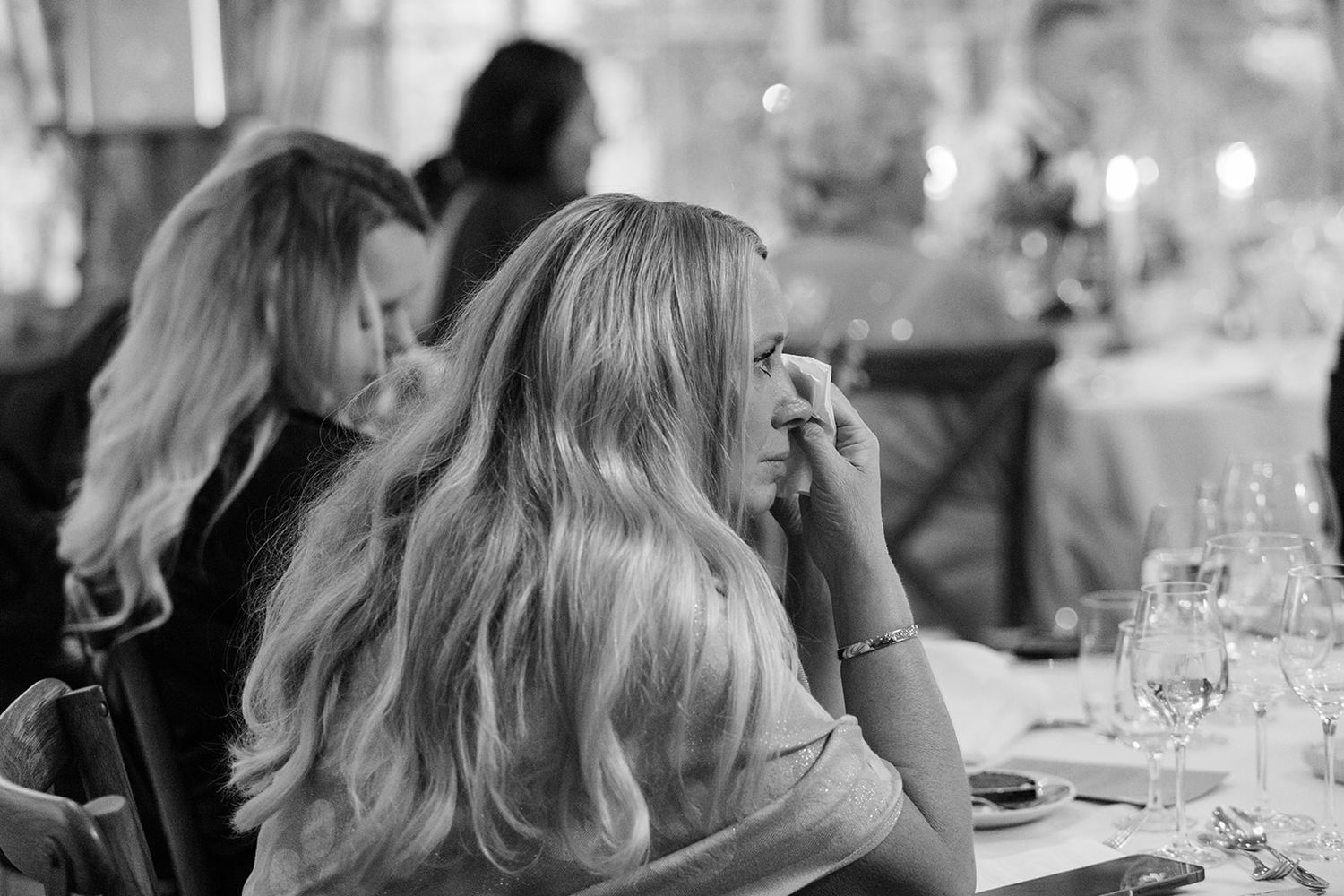 A group of people sit at a table during a formal dinner event with wine glasses and ambient lighting.