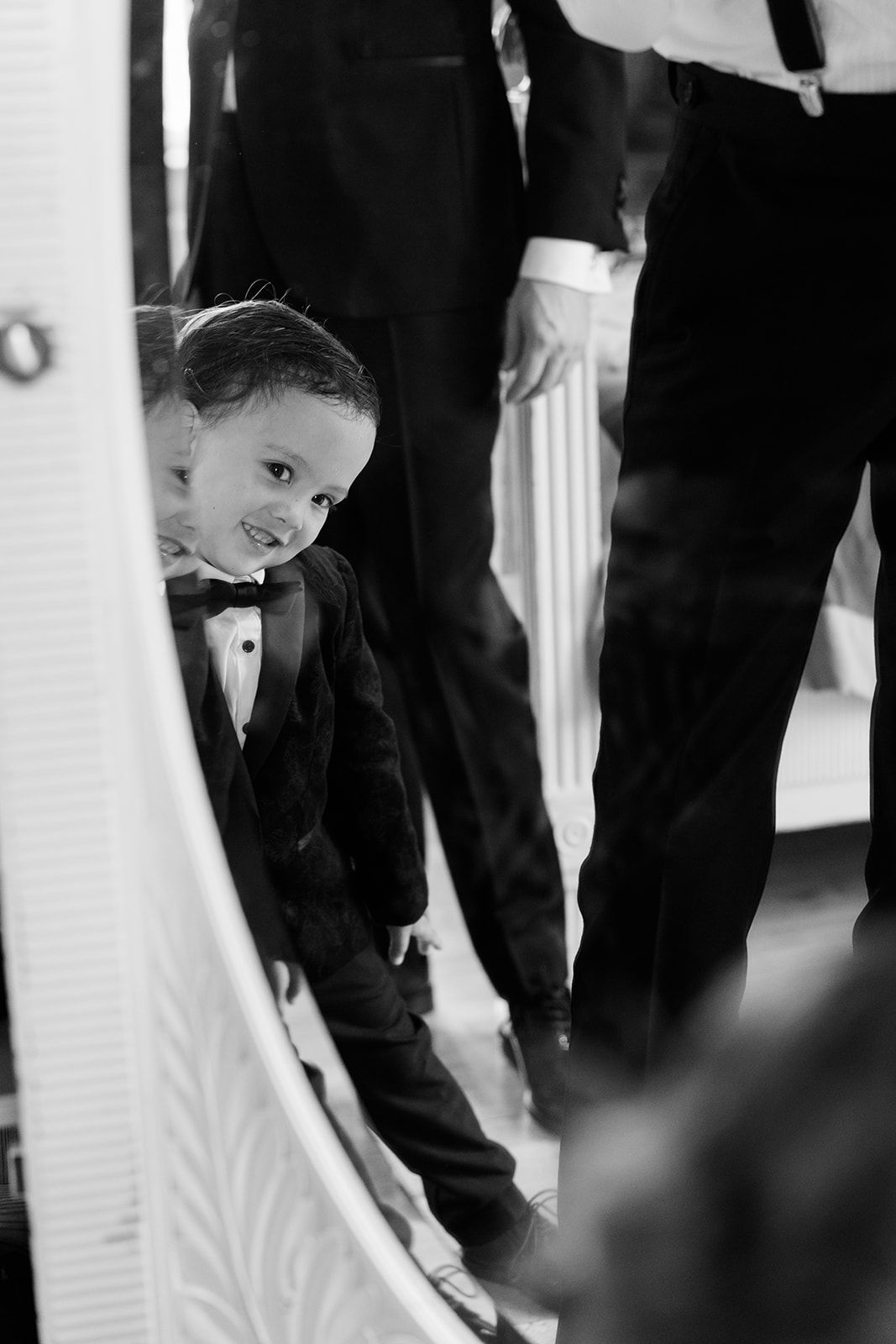 A child in formal attire bends down to adjust something near the ground during what appears to be a wedding ceremony.
