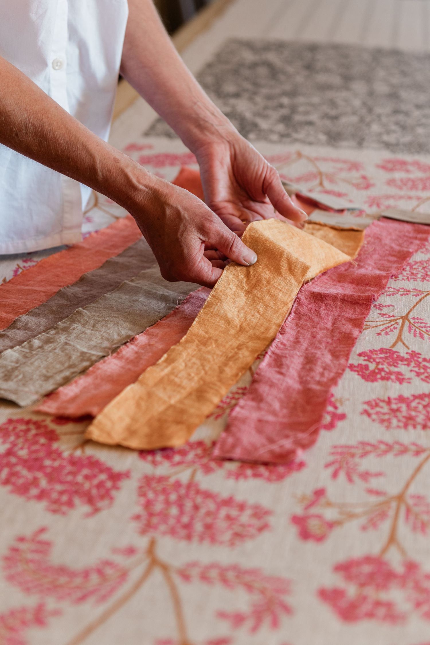 Hands carefully arranging colourful fabric strips on a floral patterned screen printed surface in the studio of Madder Cutch.