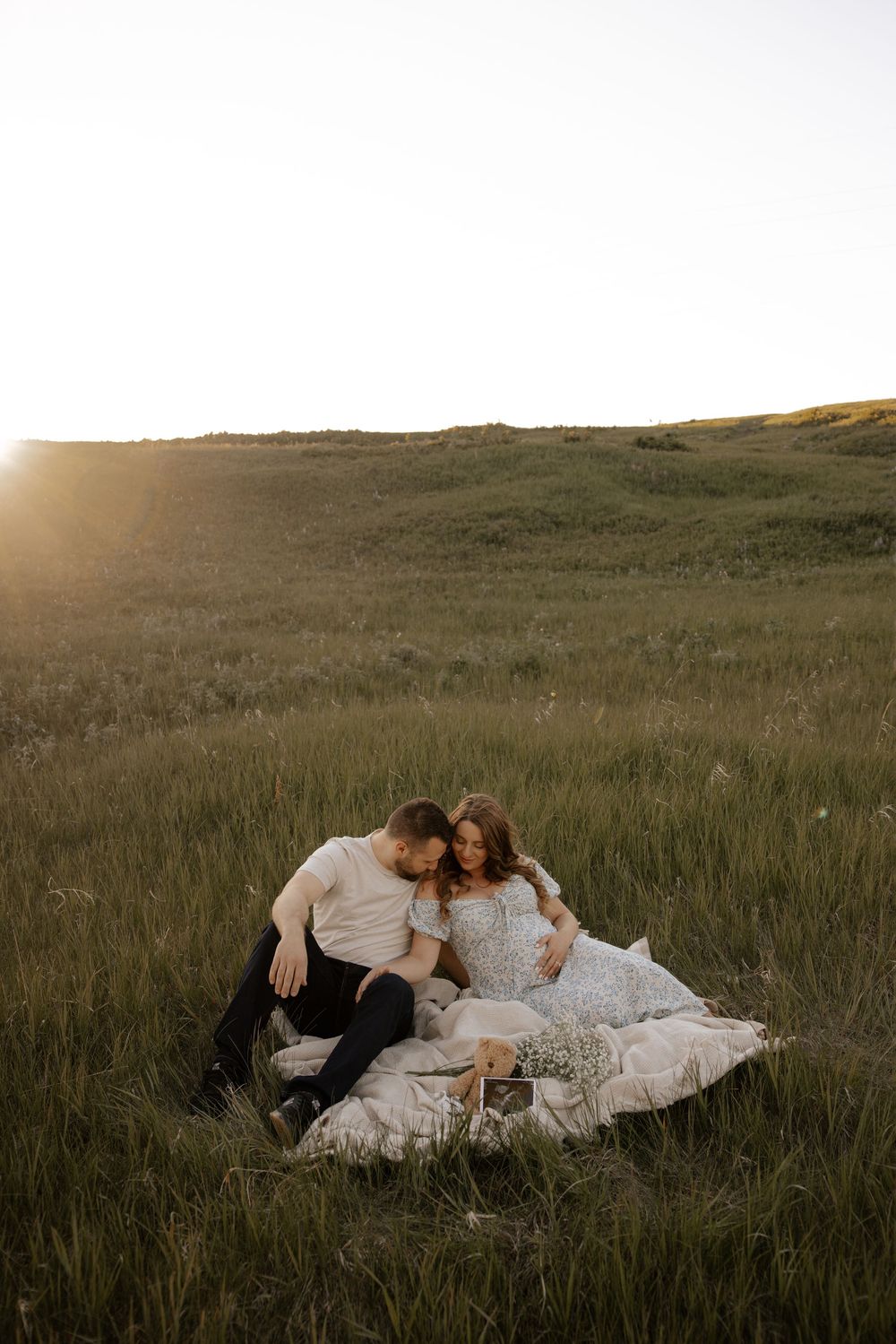 Couple sitting in a green field at golden hour while they look at their pregnancy ultrasound for their maternity pictures