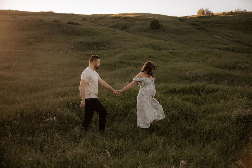 pregnant woman embraces her partner at nose hill park for her maternity photoshoot