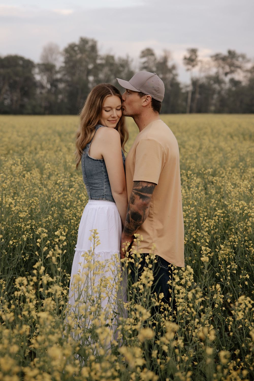 Couple embracing romantically in a yellow flower field at dusk.