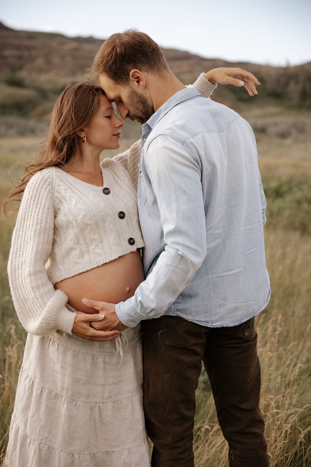 A couple shares a tender moment outdoors, in red deer alberta where they embrace their pregnancy together