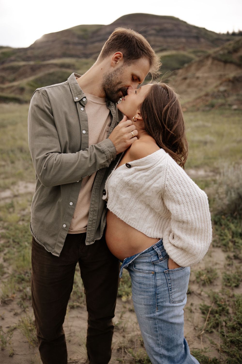 A couple shares a tender kiss outdoors, in dry buffalo jump alberta during their maternity photoshoot