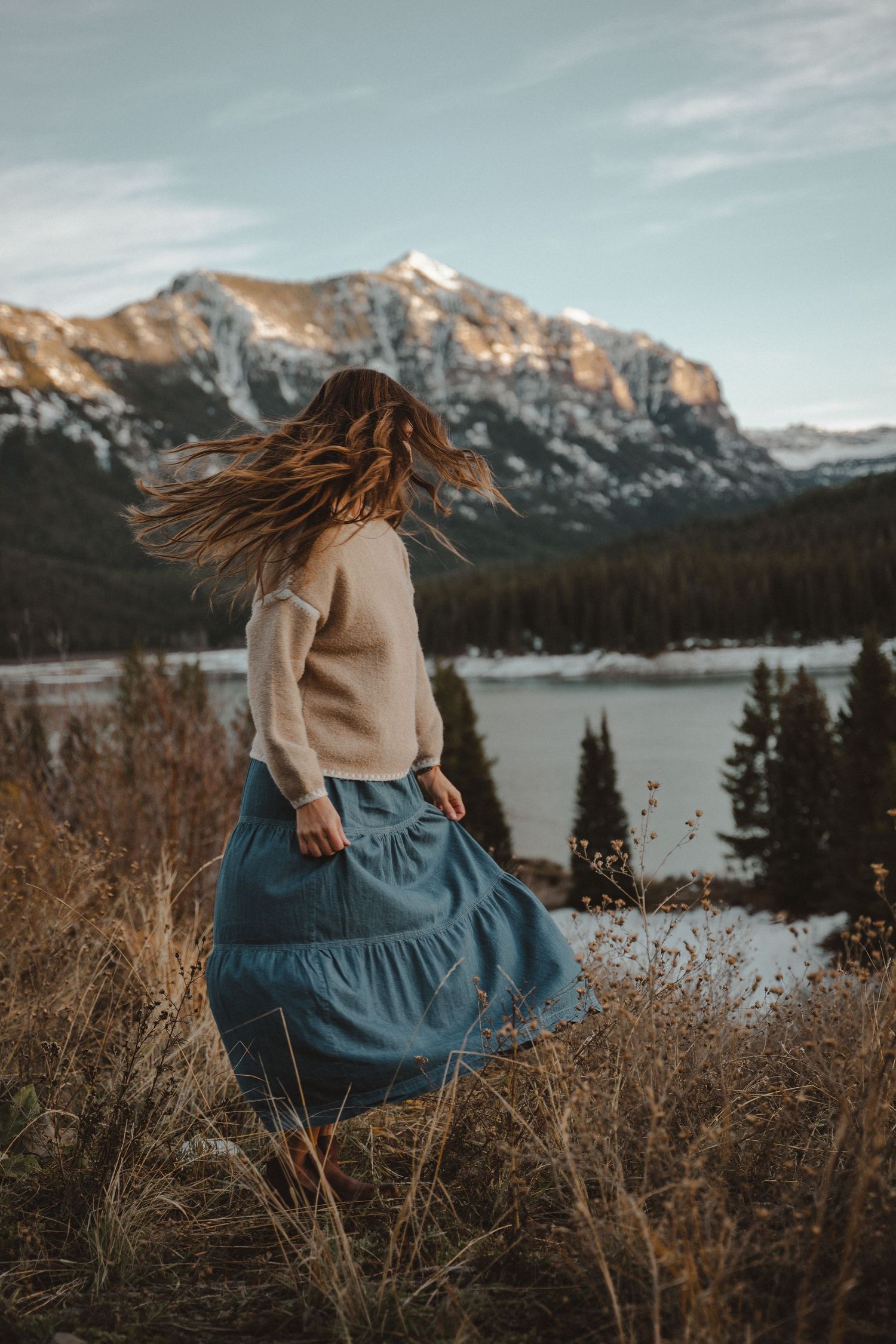 Mountain landscape with lake view and figure in blue dress sitting in dry grass.