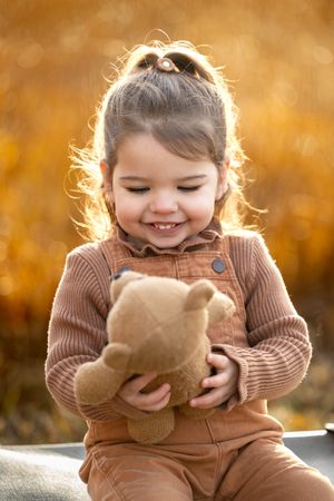 foto in bruintinten; meisje lacht naar teddybeer; kleding in bruintinten