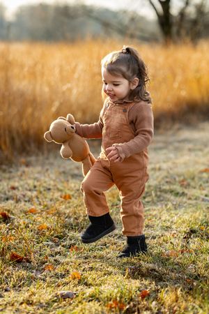 klein meisje in winterslandschap, gekleed in bruine tuinbroek met bruine coltrui. ze draagt een teddybeer