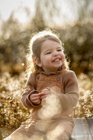 lachend meisje, gekleed in bruintinten, zittend op een oude vintage koffer; kinderportetshoot lemelerveld
