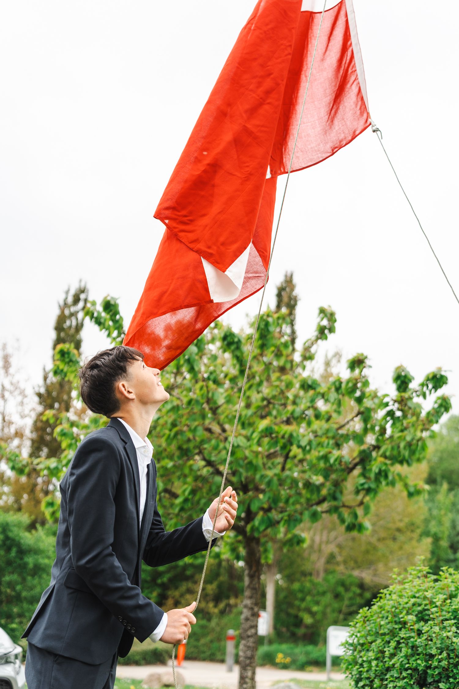 Person in business attire holds red flag against green foliage background.