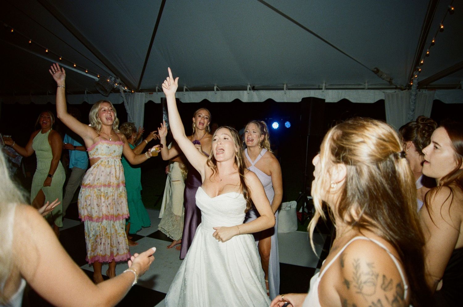 Wedding reception guests dancing and celebrating under a white tent during an evening party.