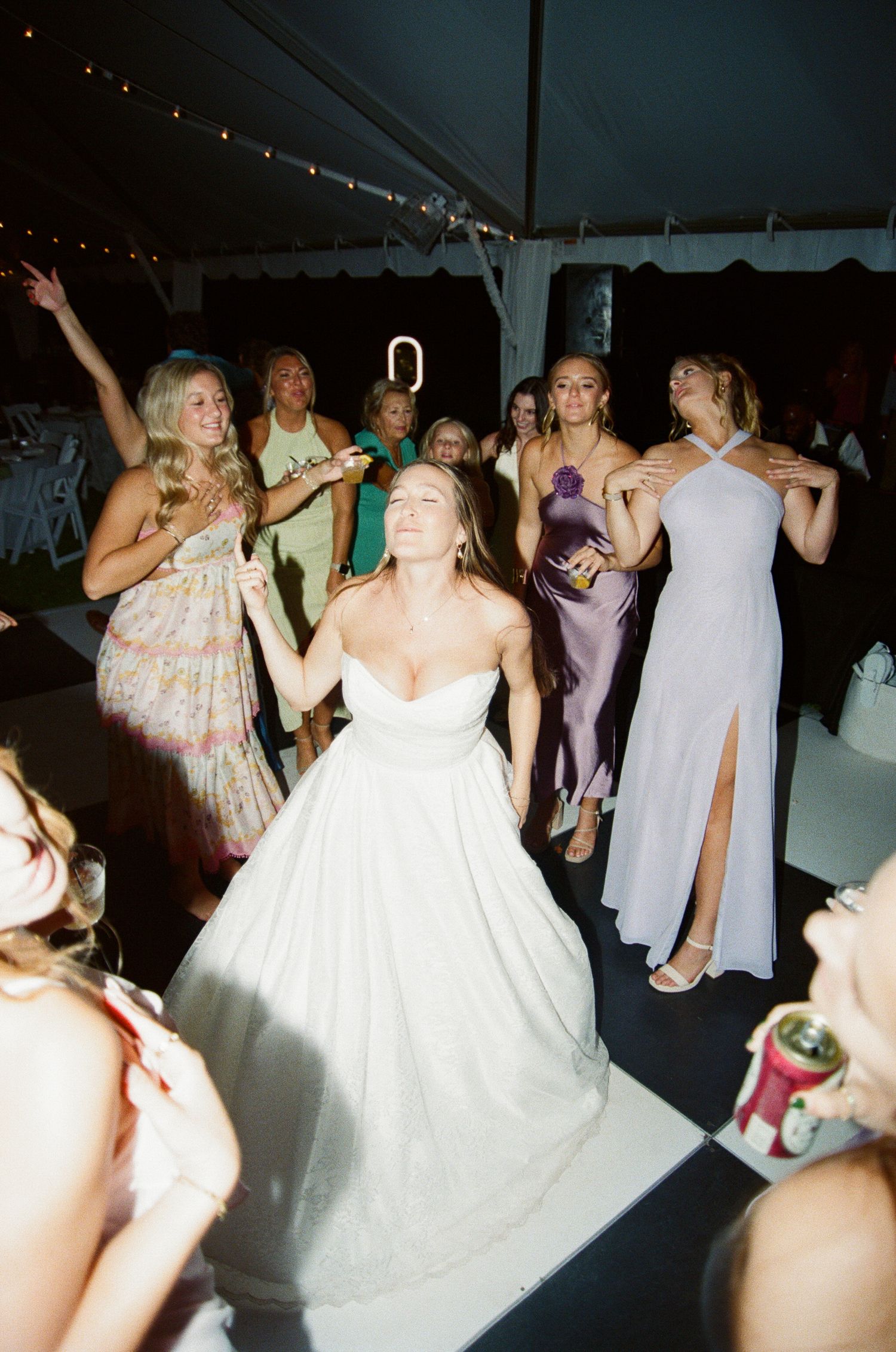 People dancing and celebrating at a wedding reception on a dark dance floor with festive lighting.