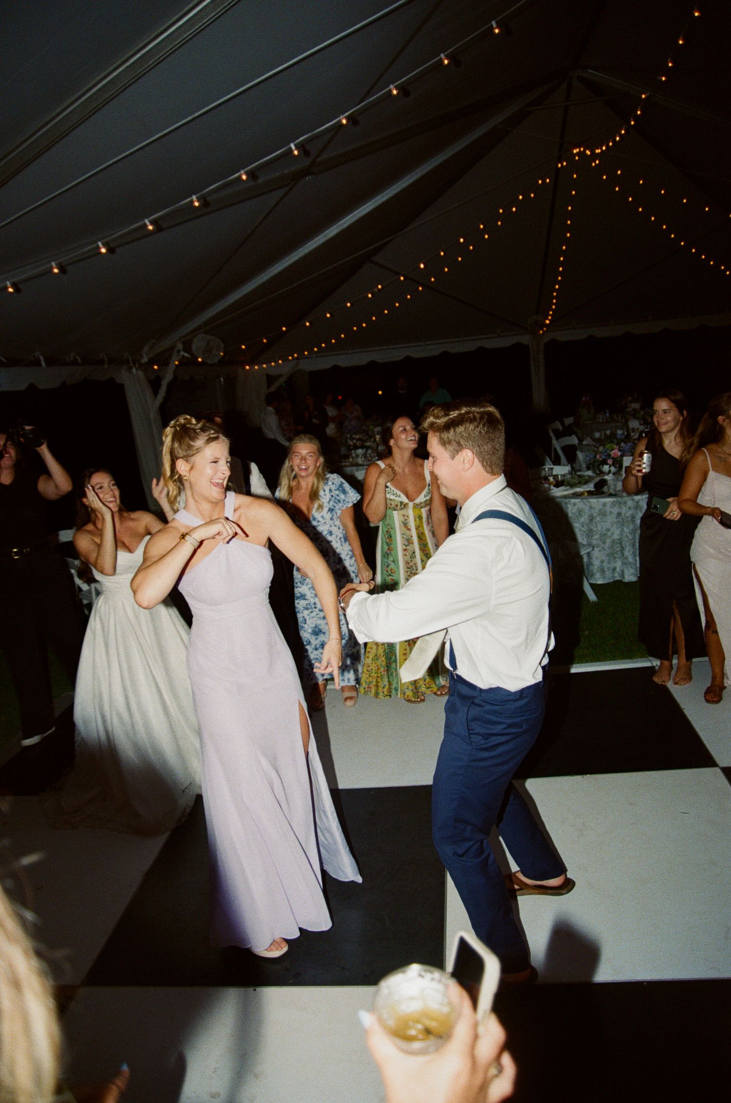 People dancing together under string lights at an evening wedding reception celebration.