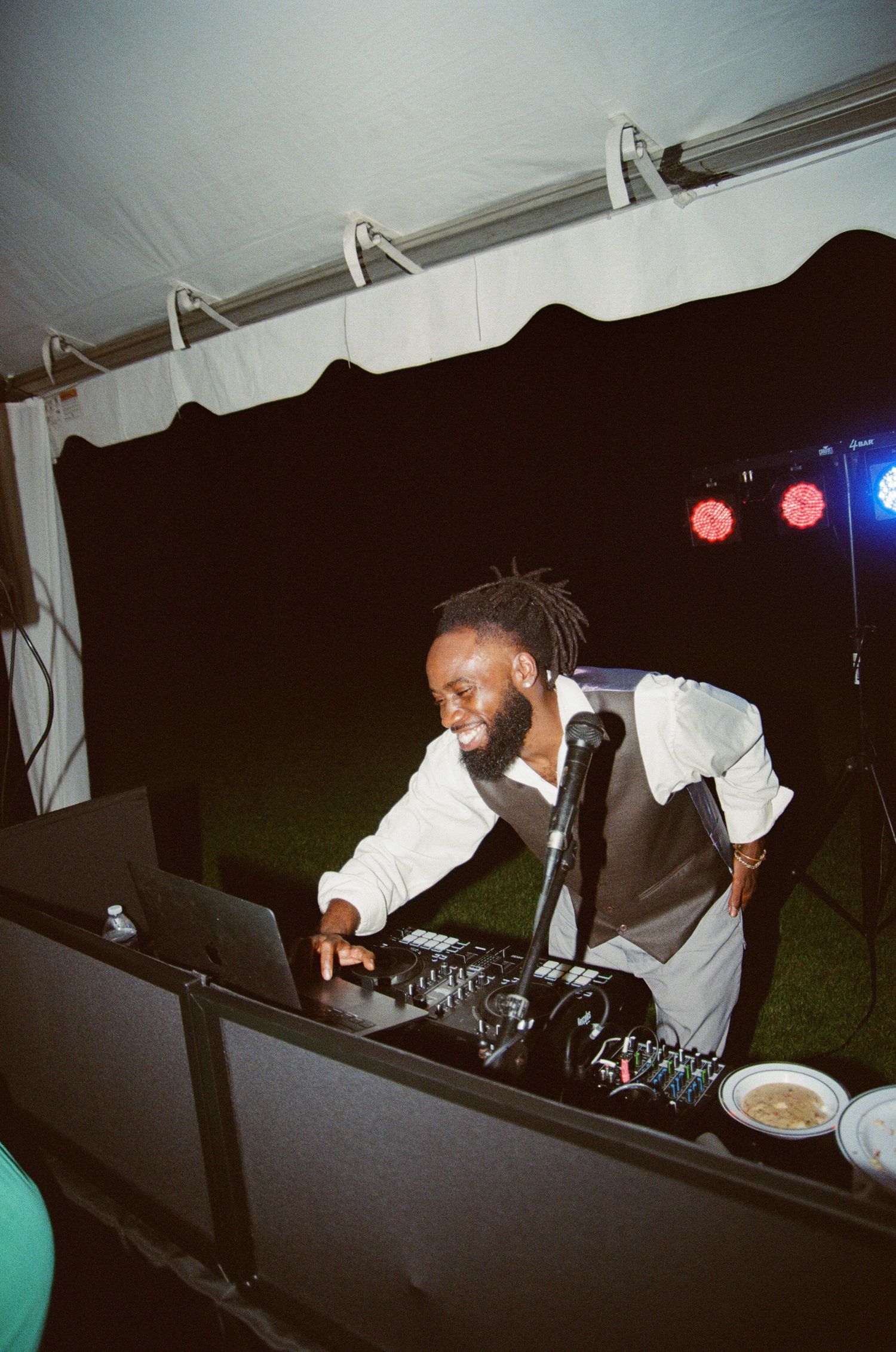 DJ performing behind booth at night event with professional equipment and lighting setup in outdoor tent venue.