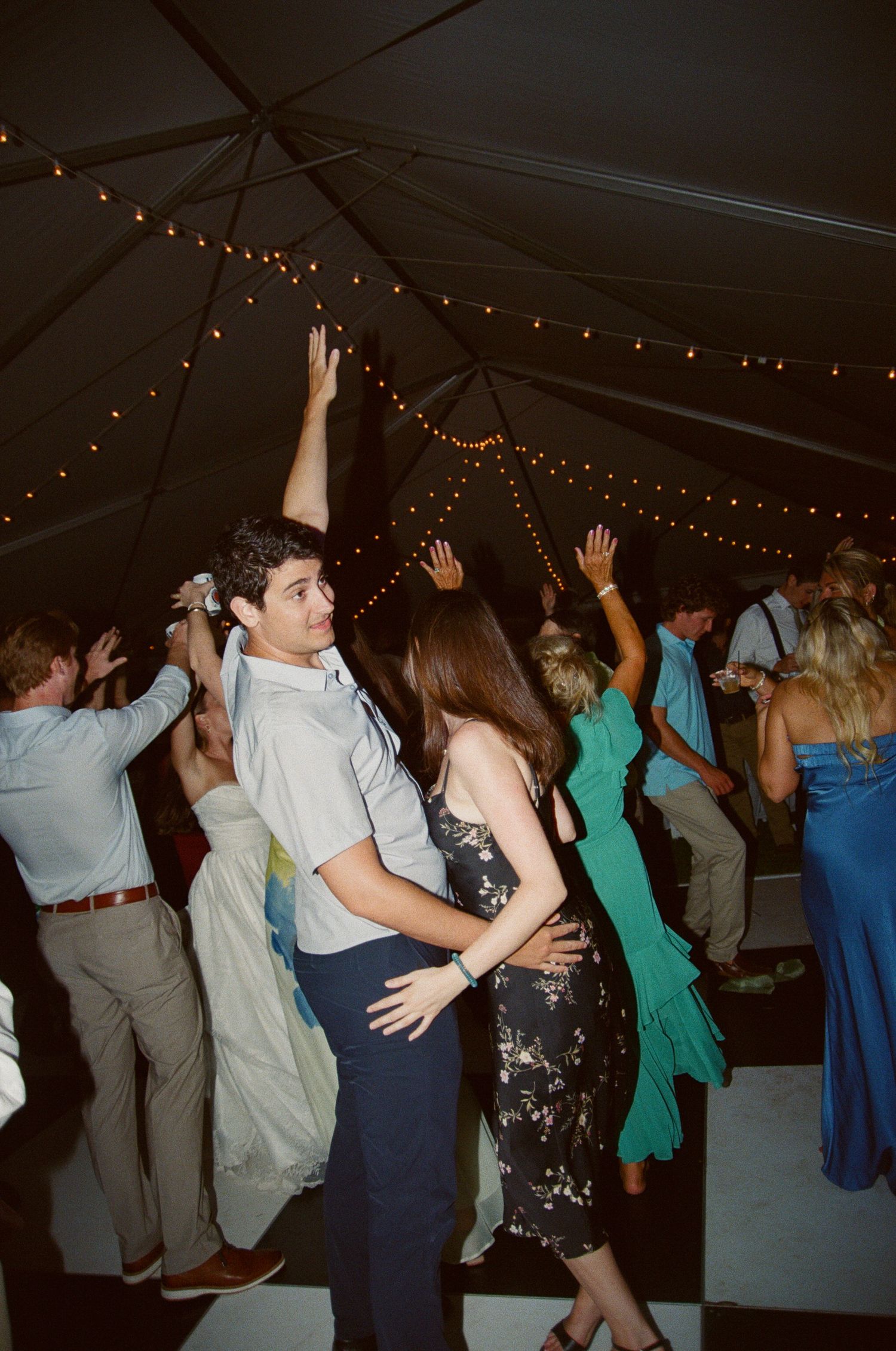 Wedding guests dancing together under string lights at an evening reception celebration.