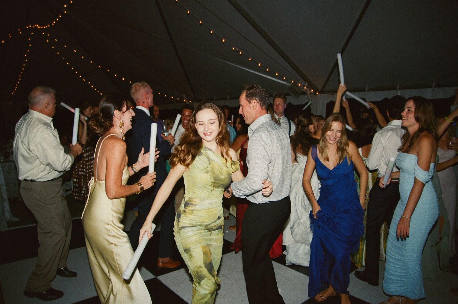 People dancing together at an evening wedding reception under string lights in a tent.