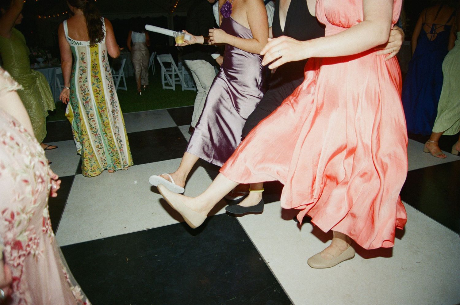Dancers in flowing pink and green dresses twirl on a dark dance floor at an evening event.
