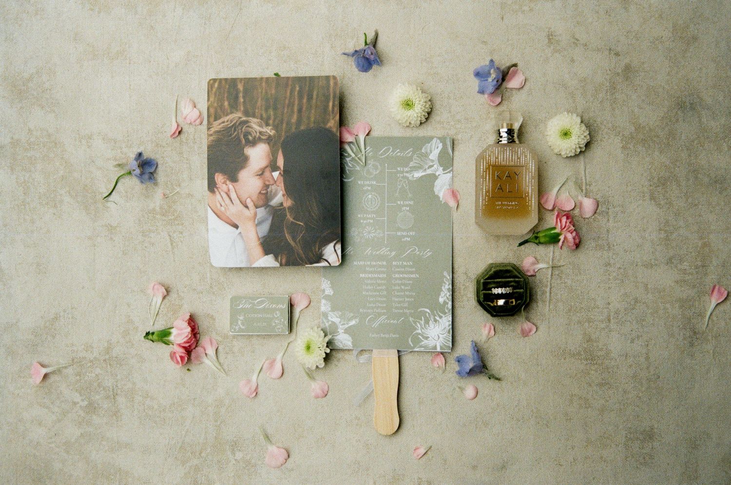 A flat lay arrangement of delicate flowers, perfume bottles, and paper pages against a textured beige background.