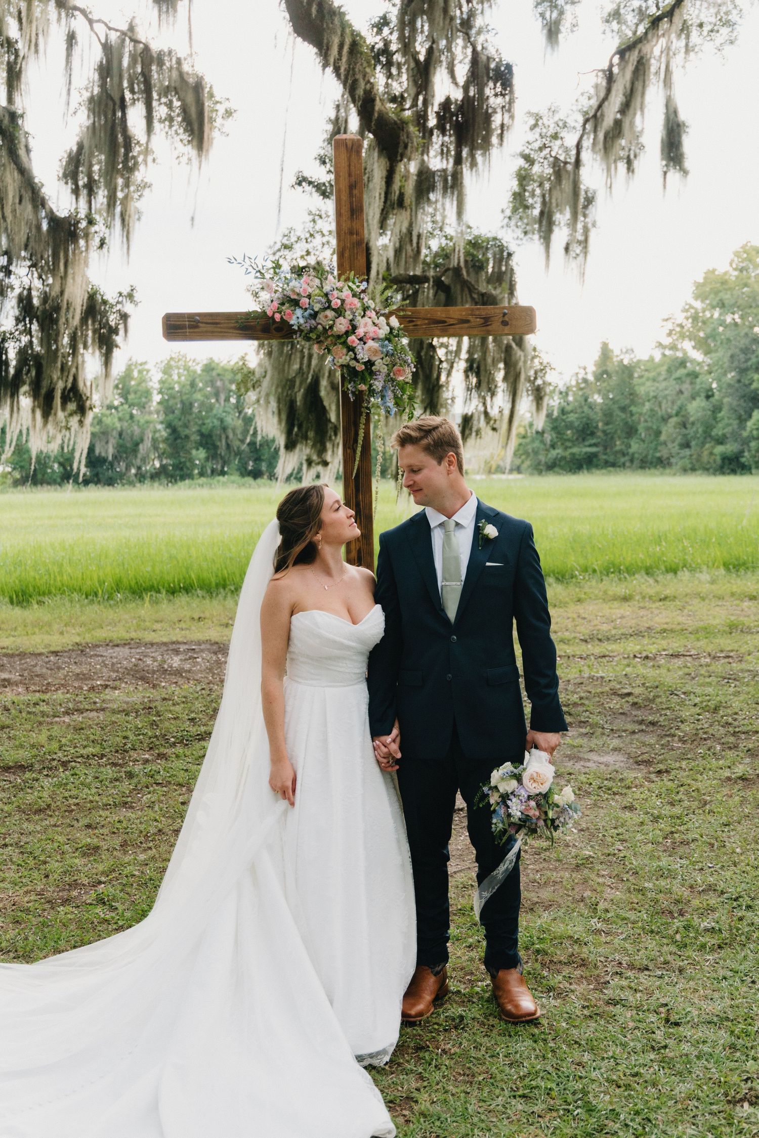 A couple shares romantic moments in a dreamy outdoor setting with Spanish moss draped trees and lush greenery.