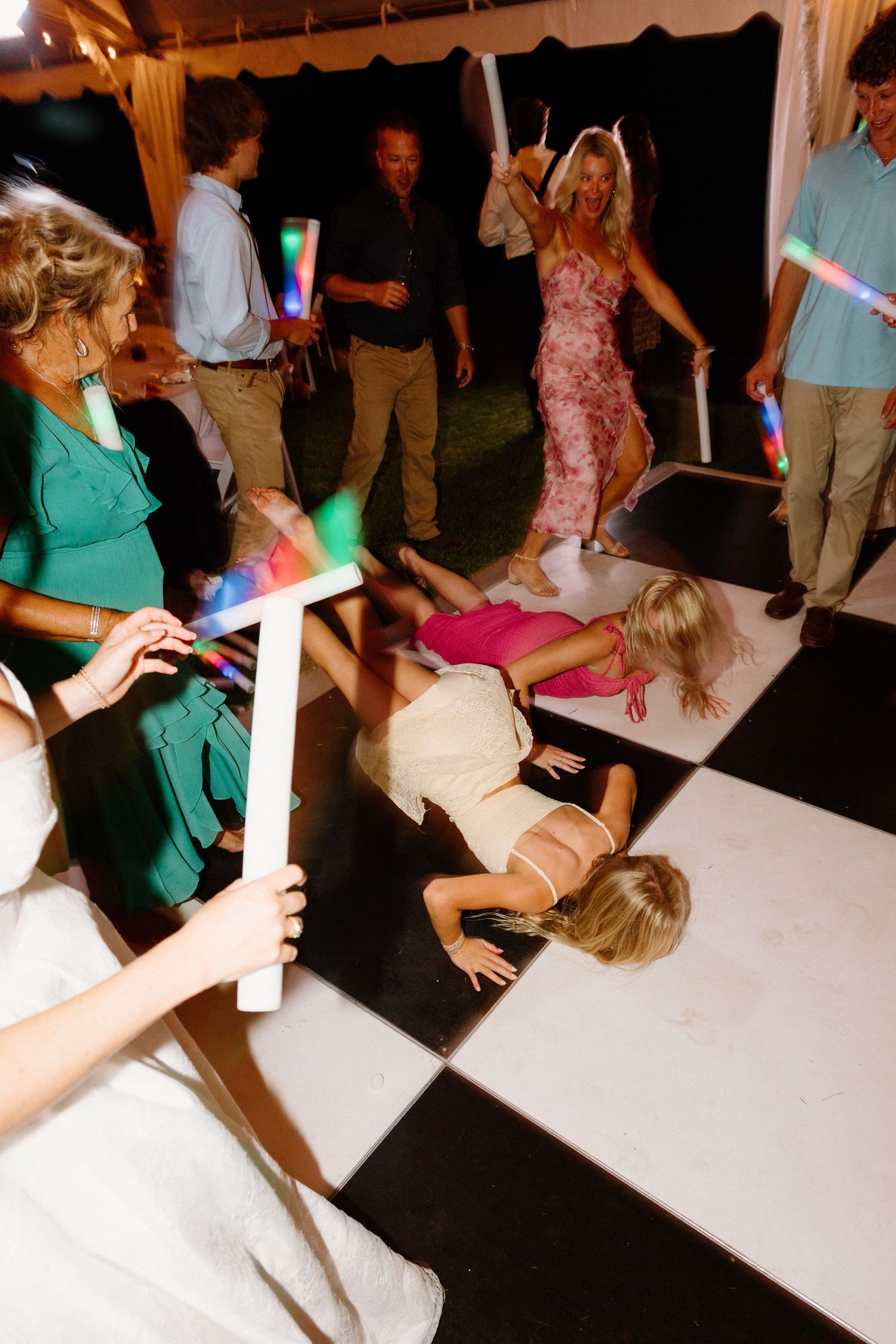 Wedding guests dance and celebrate on the dance floor while holding colorful LED light sticks at a reception party.