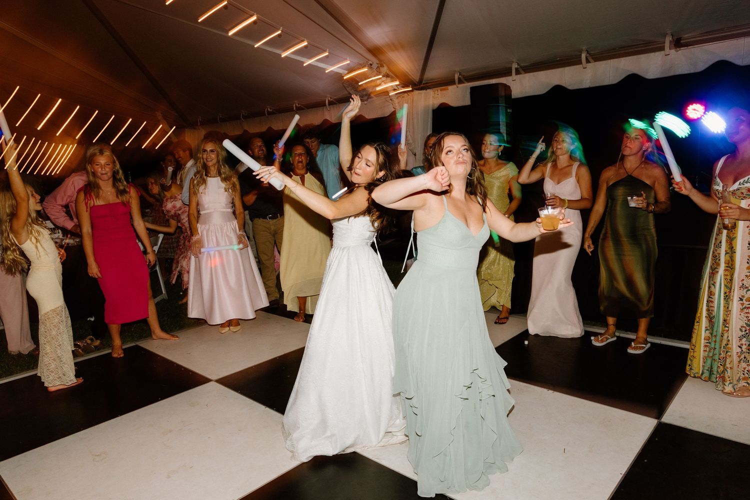 Wedding guests dance and celebrate on an illuminated dance floor during an evening reception celebration.