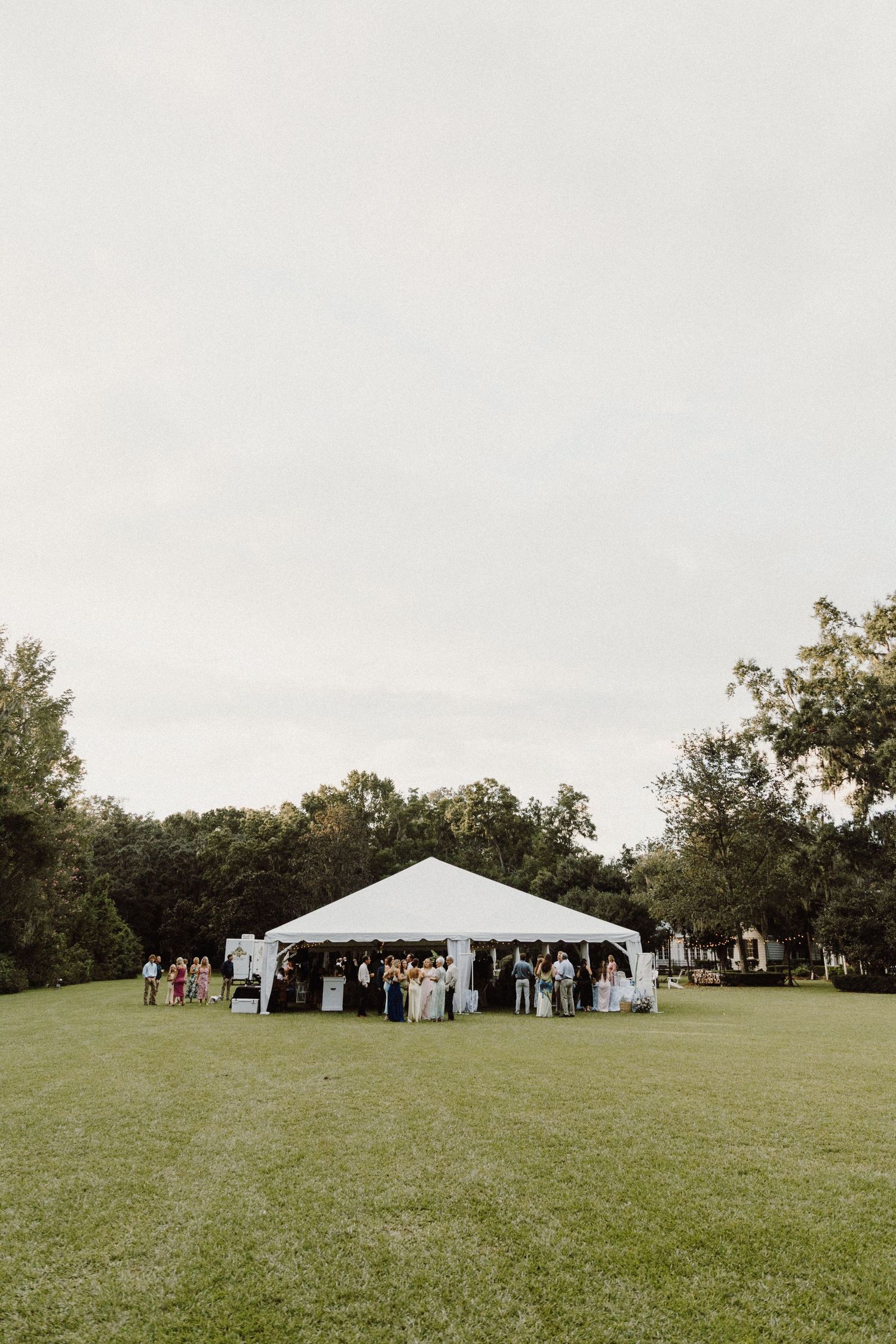 White wedding tent set up on a sprawling green lawn with trees in the background for an outdoor celebration.