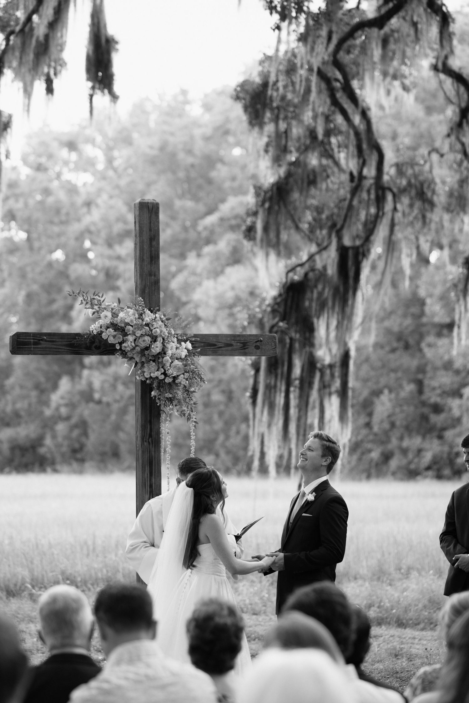 An outdoor wedding ceremony takes place under Spanish moss trees with wooden crosses in the background.