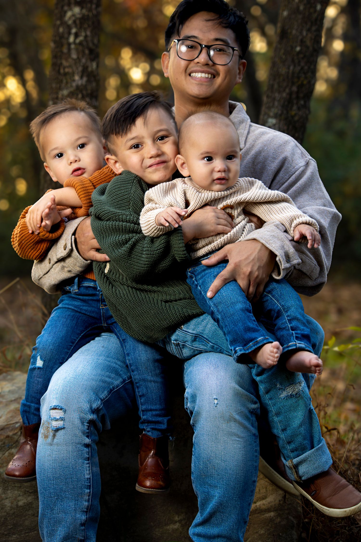 A heartwarming family portrait of a parent with three young children sitting together outdoors in autumn.