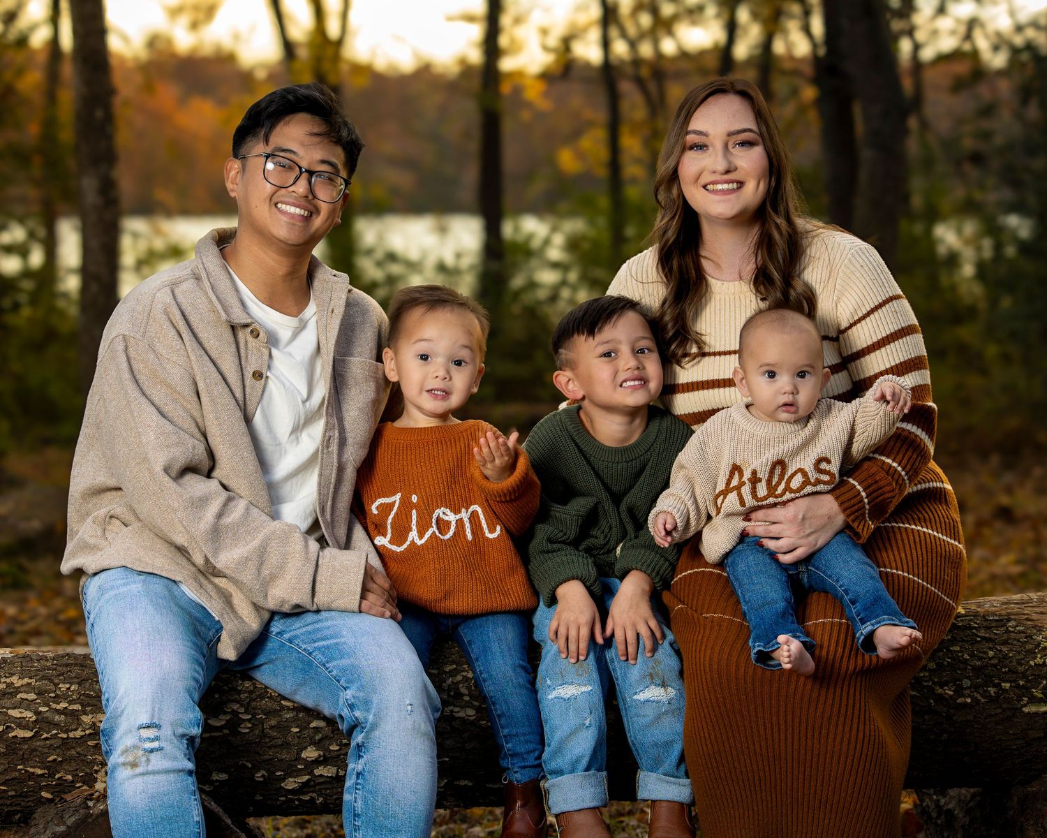Family wearing coordinating brown and denim outfits sits together on log during autumn sunset photo session in Fayetteville AR peak foliage