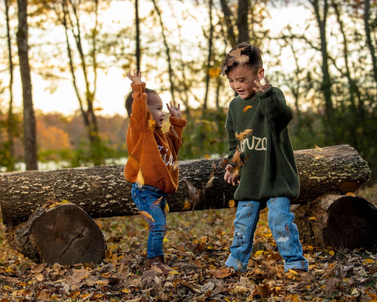 Two children playing on fallen logs in an autumn forest at sunset with golden light filtering through trees in Fayetteville AR