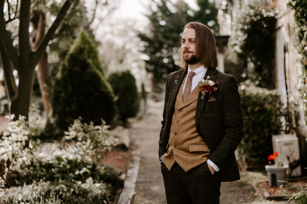 A romantic couple in formal attire embraces in a garden setting during an outdoor autumn photoshoot.