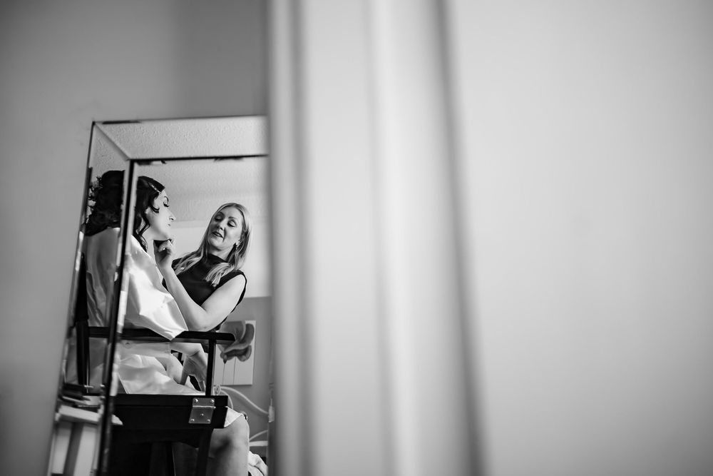 A black and white candid moment captured through a mirror reflection showing two people in an intimate pose.
