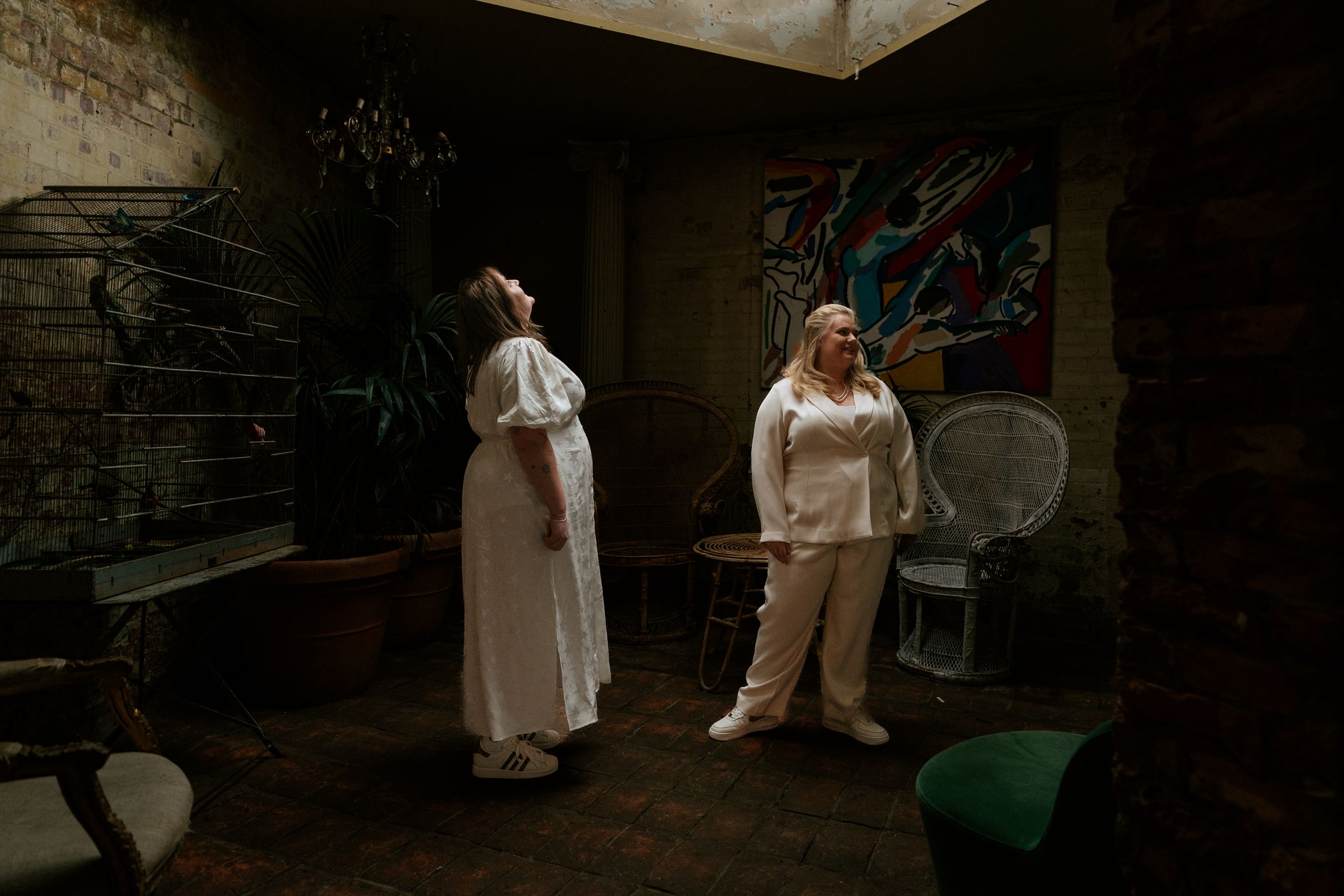 Dimly lit underground tunnel with figures in white clothing standing against stone walls and graffiti.