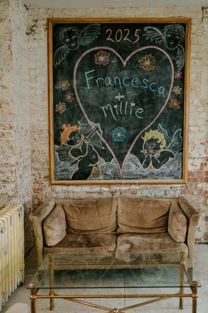 Vintage chalkboards with handwritten text hang above worn brown couches in a rustic room.