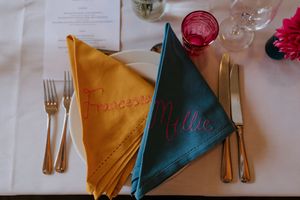 Table settings at a formal event with gold and teal napkins arranged alongside elegant place settings and glassware.