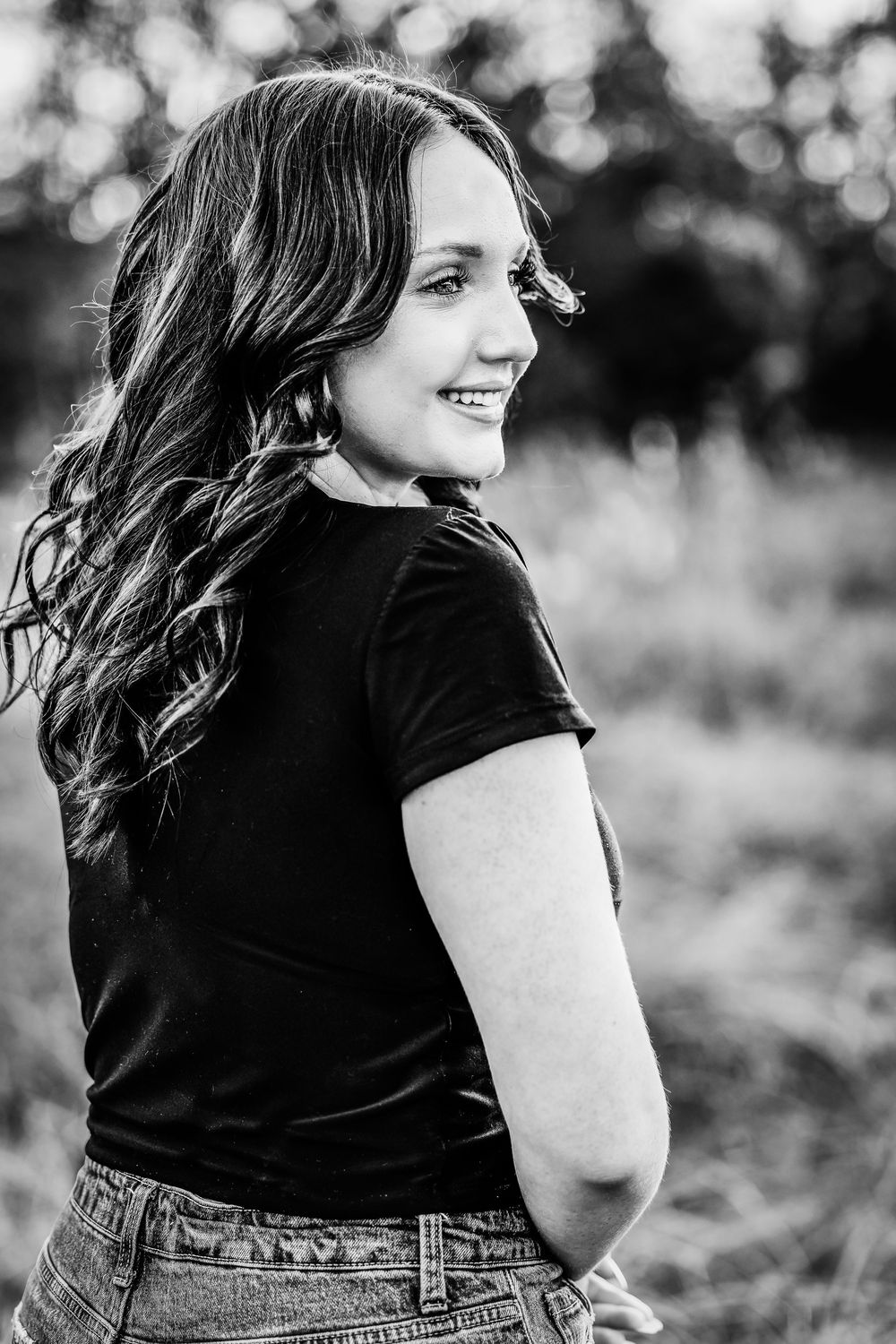 Black and white artistic portrait of a woman in a black shirt and denim, laughing outdoors in natural lighting.