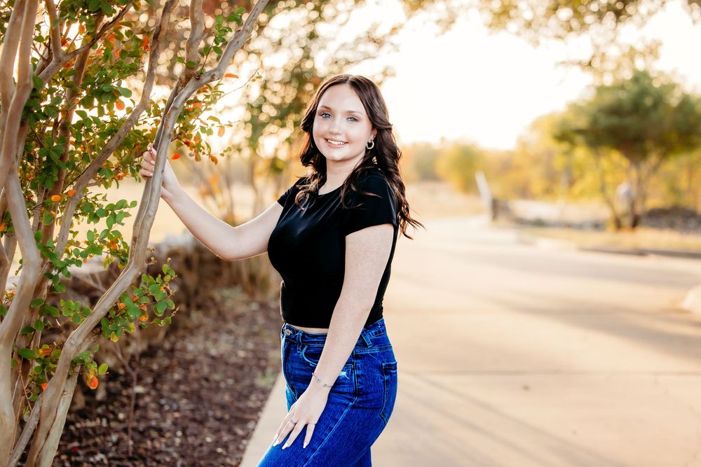 A figure in a royal blue dress poses gracefully outdoors during golden hour with trees in the background.