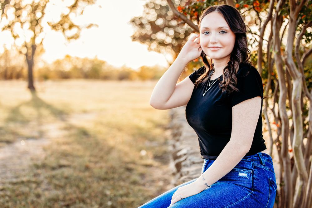 A woman in a blue dress poses outdoors during golden hour in a rustic natural setting.