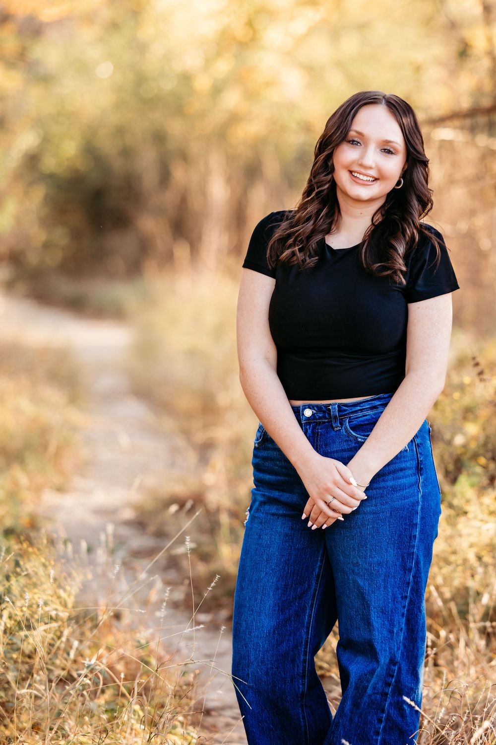 A series of outdoor portrait photos showing someone in a black top and blue jeans posing in golden sunlit grass.