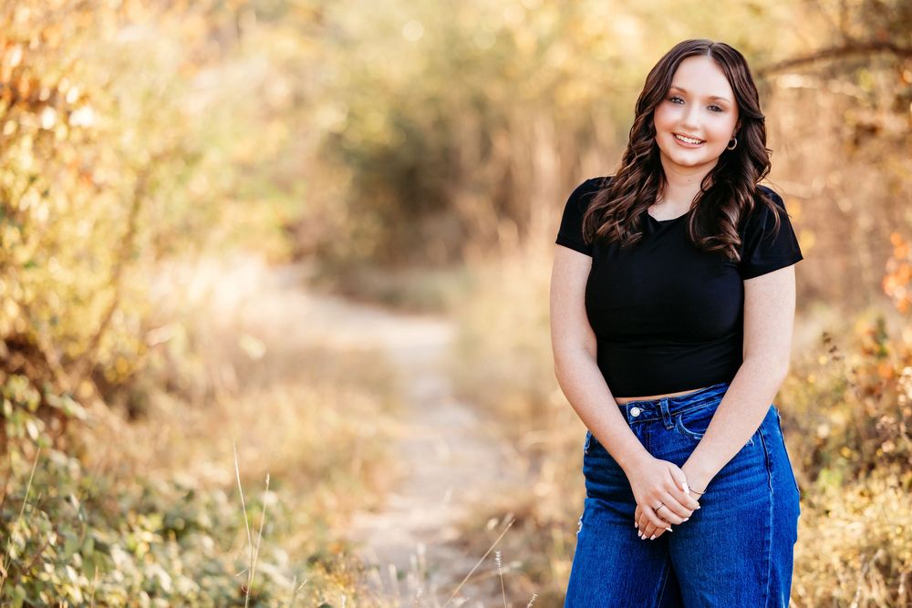 Professional outdoor portrait session in autumn with golden light and blue dress against natural foliage background.