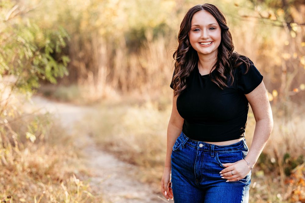 A person in casual attire poses outdoors during golden hour with autumn foliage in the background.