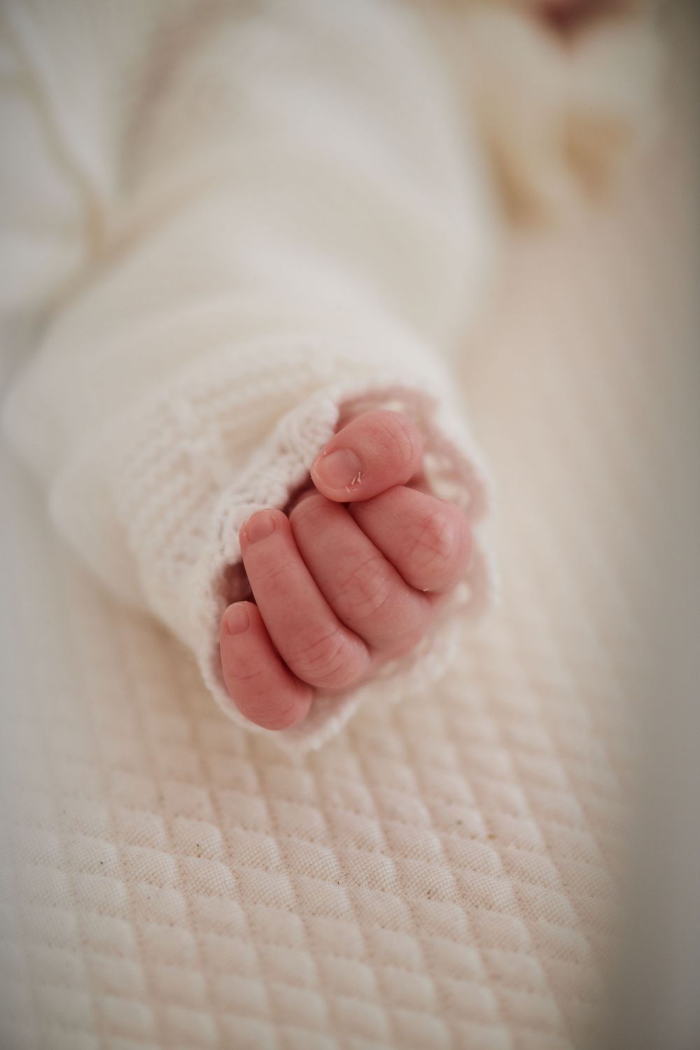Close-up of a newborn baby's tiny clenched fist in a white lace-trimmed knit sleeve.