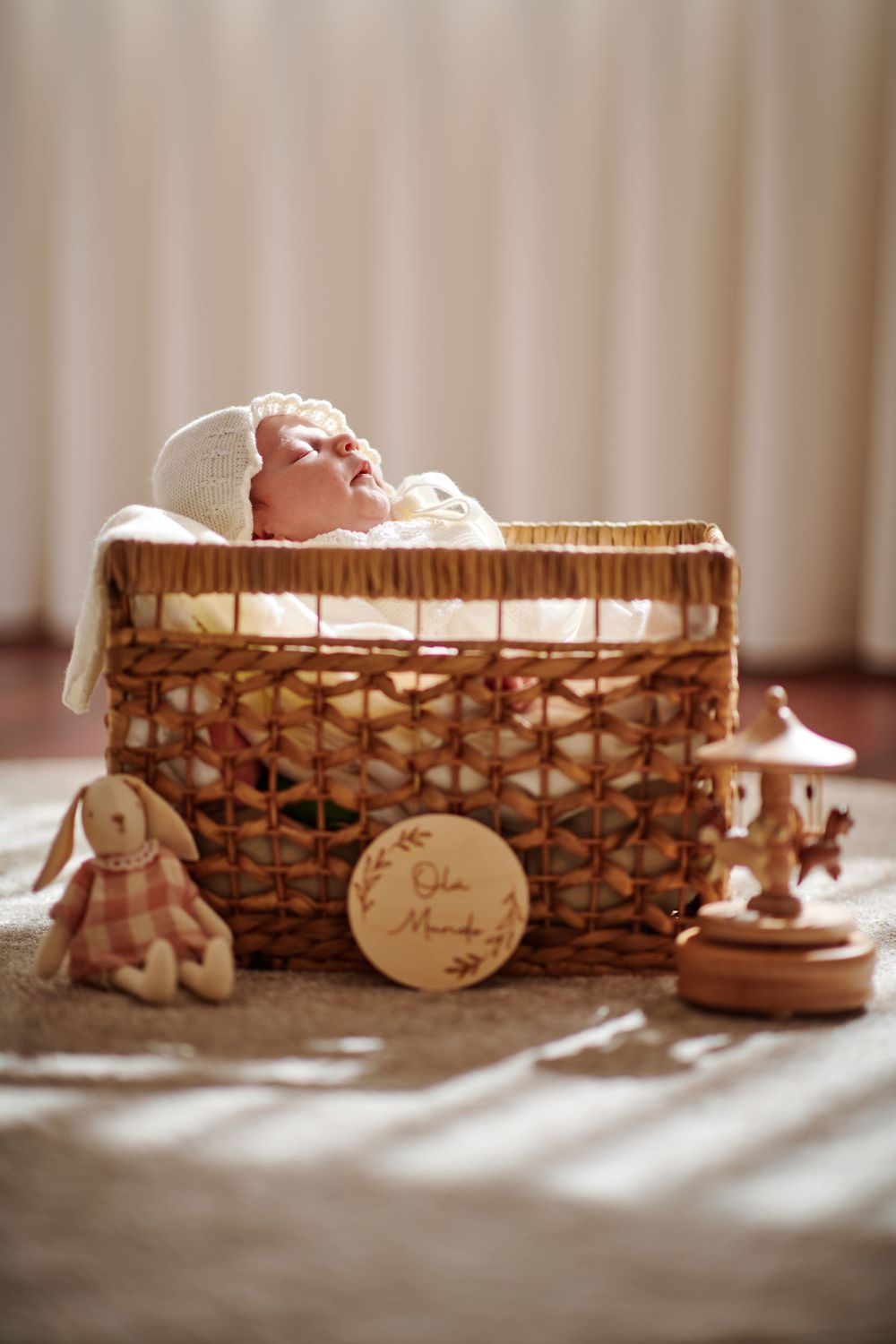 Sleeping newborn baby in a wicker basket with toys and an Ola Mundo wooden sign.